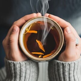 Hände halten eine Tasse Tee, um Stress im Körper zu beruhigen