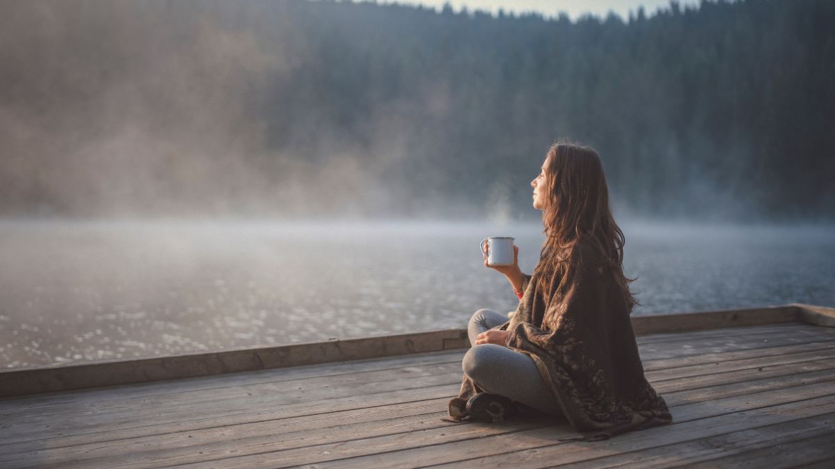 Frau sitzt am See mit einer Tasse Tee – Moment der Ruhe zur Stressreduktion