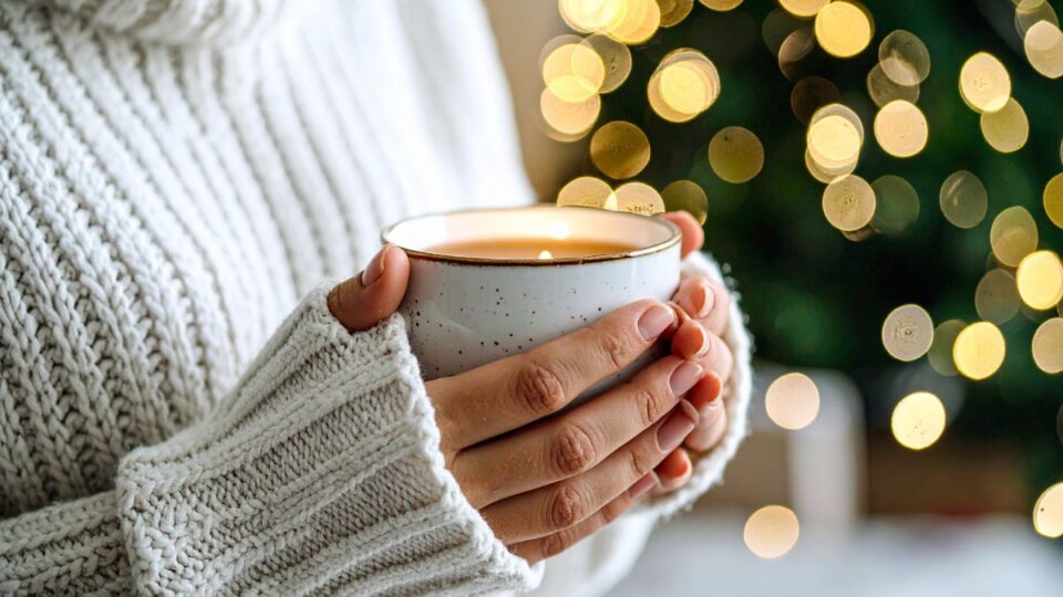 Hände halten eine warme Tasse mit Lichtern im Hintergrund – Symbol für Ruhe und Entschleunigung und Fastenzeit ohne Druck